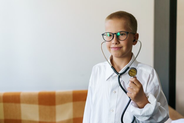 Mignon petit garçon caucasien en uniforme médical portant des lunettes avec stéthoscope jouant au docteur heureux f...