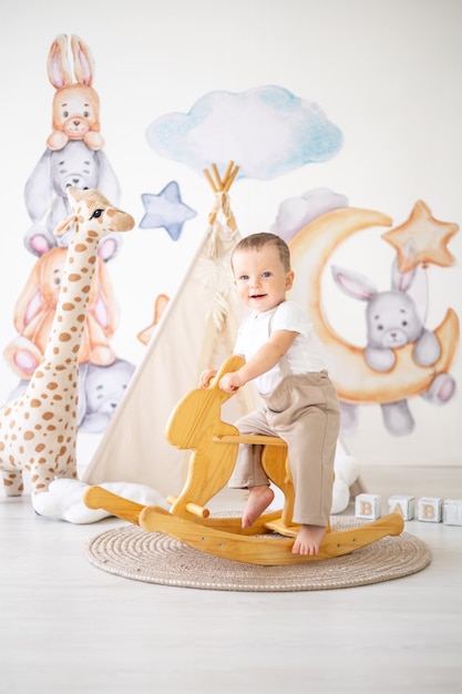 Mignon petit garçon chevauche un lièvre à bascule en bois dans la chambre des enfants à la maison jouets éducatifs pour enfants
