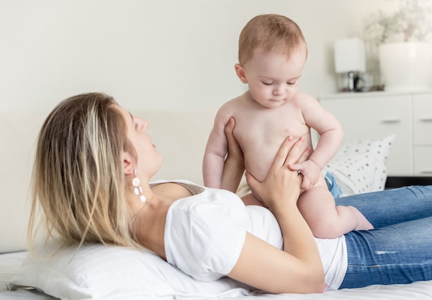 Mignon petit garçon en couches assis sur la mère allongée sur le lit