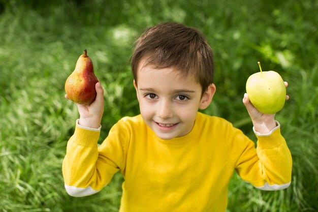 Mignon petit garçon cueillir des pommes dans un fond d'herbe verte à une journée ensoleillée