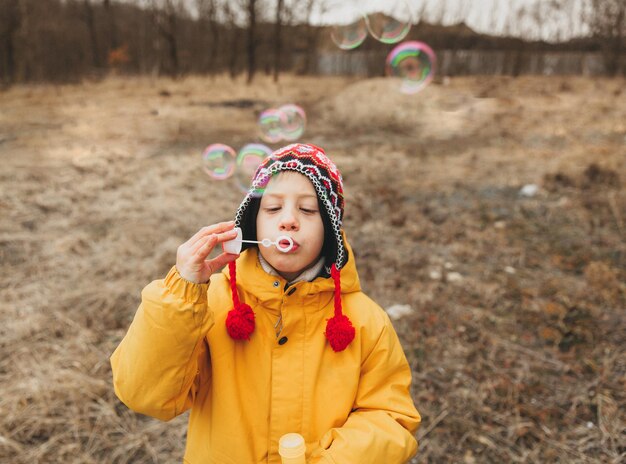 Mignon petit garçon dans un bonnet tricoté souffle des bulles de savon dans le parc d'automne.