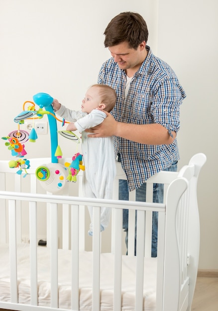 Mignon petit garçon debout dans un lit bébé et jouant avec un carrousel avec son père