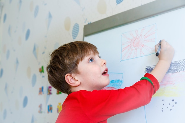 Mignon petit garçon dessinant sur un tableau blanc avec un feutre et souriant Concept d'éducation précoce