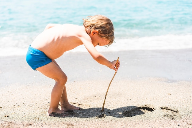 Mignon petit garçon drôle jouant avec du sable au bord de la mer été plage vacances enfance mode de vie holi...