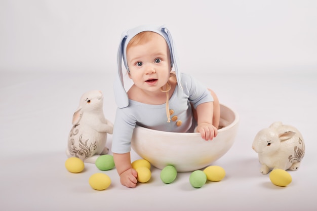 Mignon petit garçon drôle avec des oreilles de lapin et des oeufs de Pâques colorés et des lapins. Bébé de Pâques. Modèle de carte de voeux de Pâques.