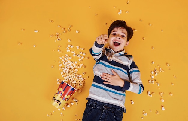 Mignon petit garçon avec du pop-corn allongé sur le sol jaune.