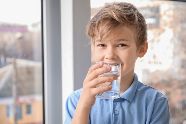 Mignon petit garçon eau potable près de la fenêtre