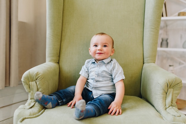 Mignon petit garçon enfant en bas âge assis dans un fauteuil vert