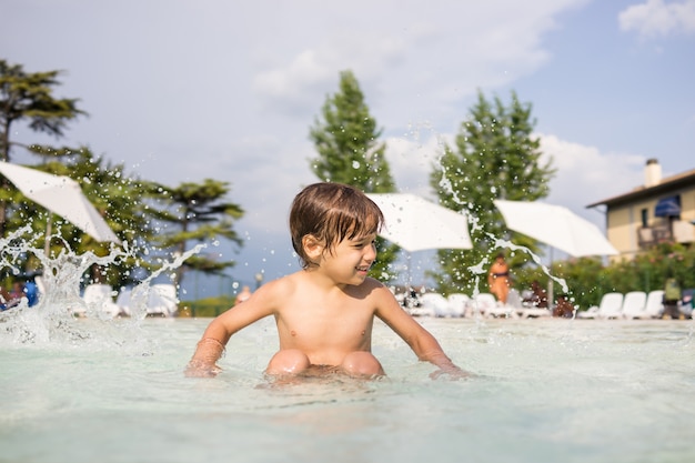 Mignon petit garçon enfant enfant éclaboussant dans la piscine s&#39;amuser activité de loisirs