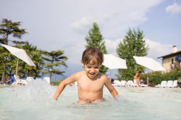 Mignon petit garçon enfant enfant éclaboussant dans la piscine s&#39;amuser activité de loisirs