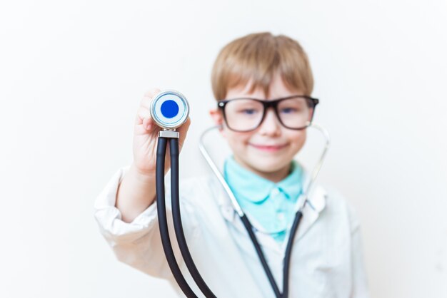 Mignon petit garçon enfant porter des lunettes d'uniforme médical tenant un stéthoscope jouant au docteur