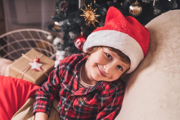 Mignon petit garçon enfant souriant au chapeau rouge attendant le père noël dans le salon avec arbre de noël