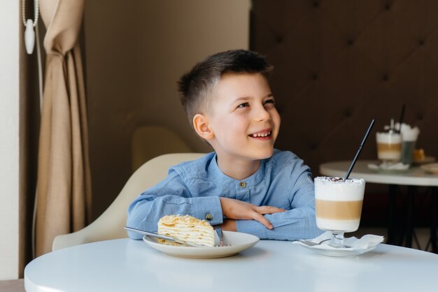 Un mignon petit garçon est assis dans un café et regarde un gros plan de gâteau et de cacao. Régime alimentaire et nutrition adéquate.