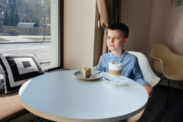 Un mignon petit garçon est assis dans un café et regarde un gros plan de gâteau et de cacao. Régime alimentaire et nutrition adéquate.