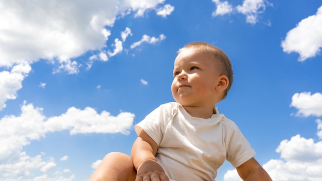 Photo un mignon petit garçon est assis sur une journée ensoleillée regardant au loin enfant heureux sur le fond du ciel d'été bleu avec des nuages concept d'imagination de rêve d'enfance