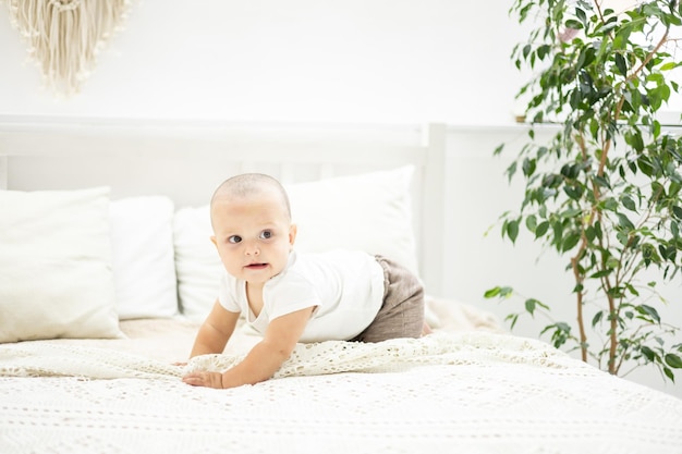 Mignon petit garçon est assis sur un lit avec des draps blancs dans la chambre de la maison le portrait d'un enfant l'enfant regarde la caméra