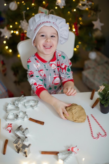 Mignon petit garçon faisant des biscuits de Noël sur un tableau blanc près de l'arbre de Noël avec des lumières Concept de cuisine de Noël