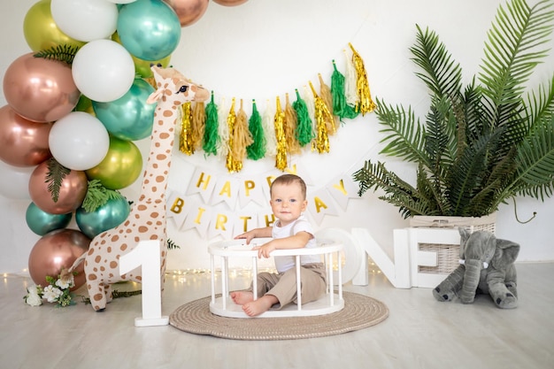 Un mignon petit garçon fête son premier anniversaire sur fond de ballons aux couleurs vives et d'accessoires festifs pour les premières vacances des enfants