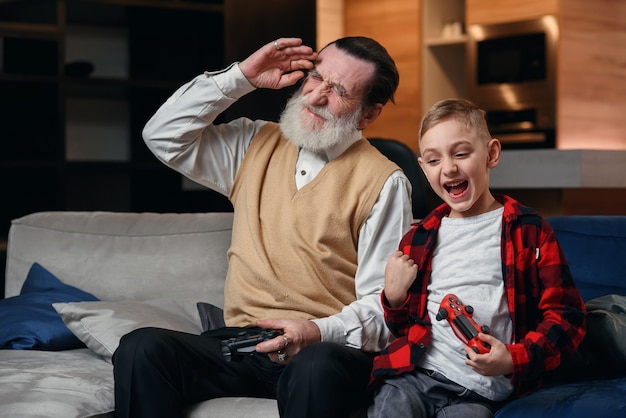 Mignon petit garçon avec grand-père assis sur un canapé et jouer à un jeu vidéo avec une manette de jeu