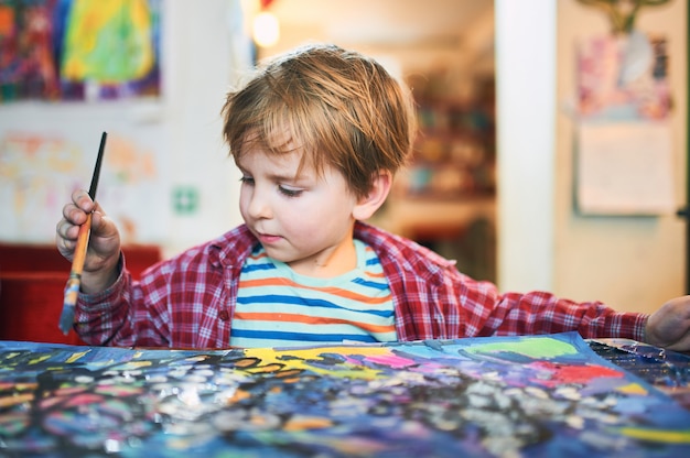 Mignon petit garçon heureux, adorable enfant d'âge préscolaire, peinture dans un studio d'art ensoleillé.