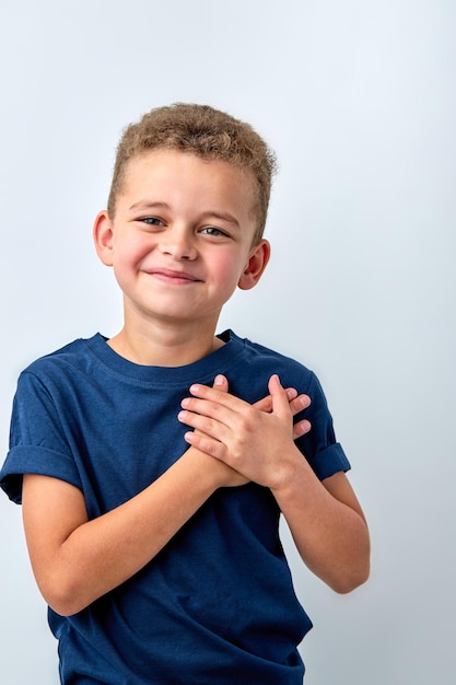 Photo mignon petit garçon heureux isolé sur fond de studio blanc tenir la main au cœur