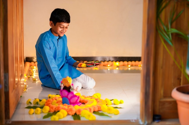 Mignon petit garçon indien faisant une décoration avec une fleur et une lampe à huile pour le festival de diwali à la maison