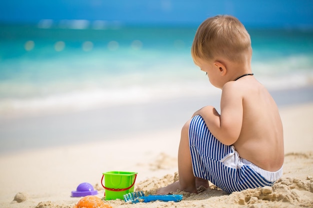 Mignon petit garçon jouant avec des jouets de plage sur la plage tropicale