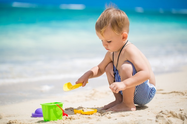 Mignon petit garçon jouant avec des jouets de plage sur la plage tropicale