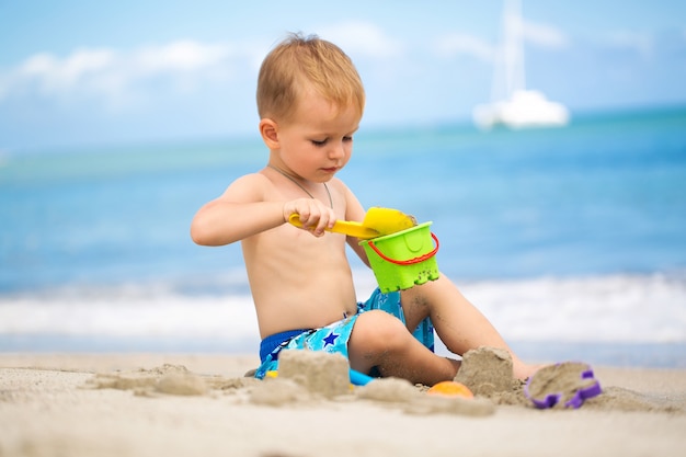 Mignon petit garçon jouant avec des jouets de plage sur la plage tropicale