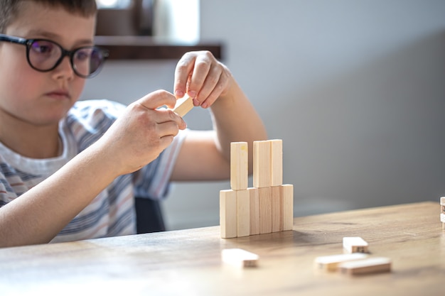 Un mignon petit garçon joue à un jeu de société avec des cubes en bois et une tourelle.