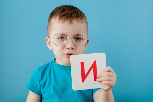 Mignon petit garçon avec lettre sur fond bleu Enfant apprenant un alphabet de lettres