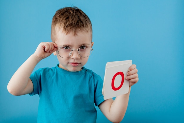 Mignon petit garçon avec une lettre sur le mur bleu. Enfant apprenant une lettre. Alphabet