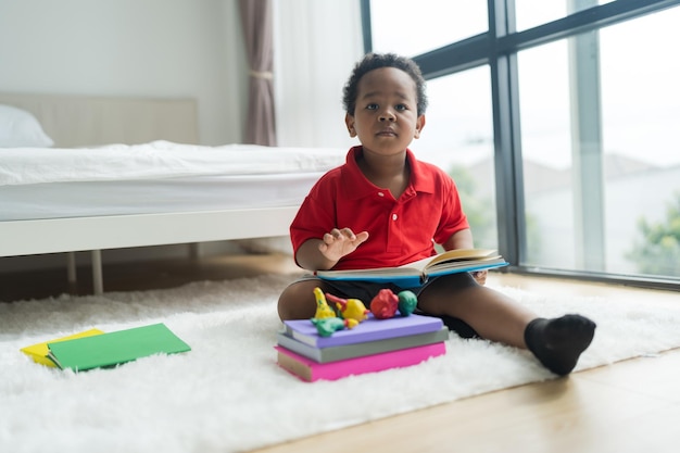 Mignon petit garçon lisant un livre sur un sol blanc dans la chambre