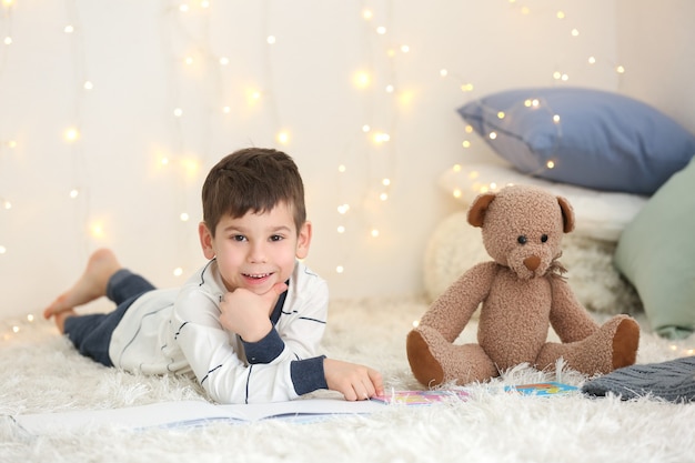 Mignon petit garçon avec un livre de lecture d'ours en peluche à la maison