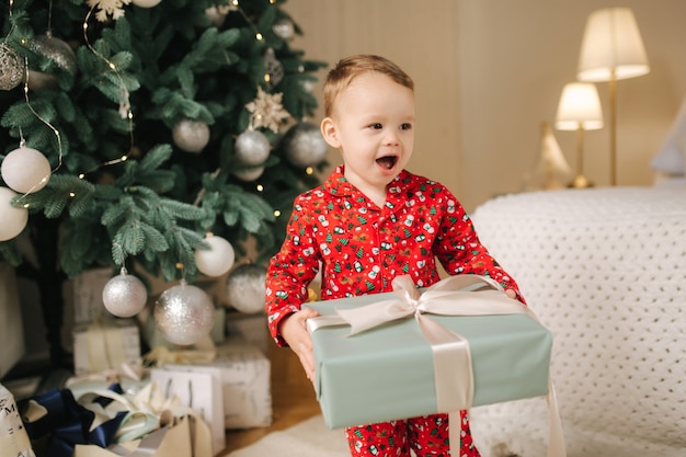 Mignon petit garçon à la maison près du grand arbre de Noël à la recherche de cadeaux. Un enfant heureux passe du temps en vacances et profite de chaque instant. Seul à la maison.