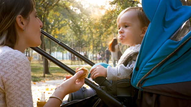 Mignon petit garçon mangeant et regardant sa mère dans le parc en automne.
