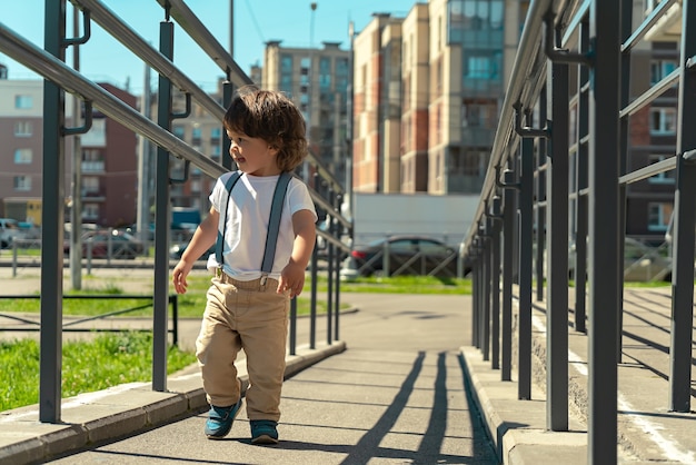 Mignon petit garçon marchant le long de la rampe à l'extérieur dans la rue de la ville