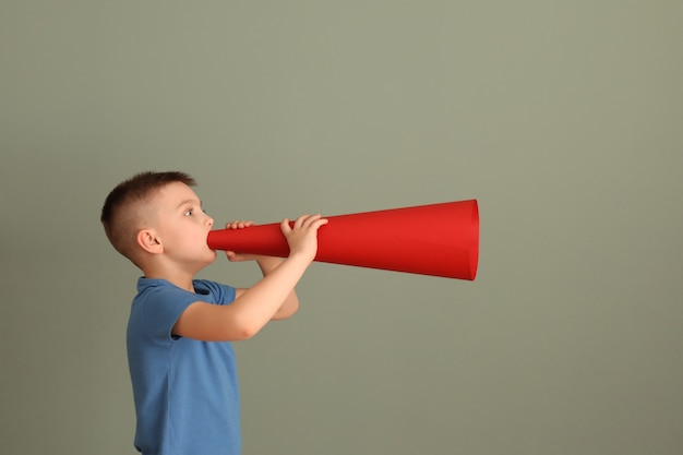 Mignon petit garçon avec mégaphone en papier sur la couleur