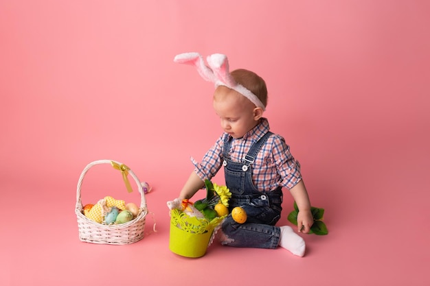 Mignon petit garçon avec des oreilles de lapin et des oeufs de pâques sur fond rose Joyeuses Pâques