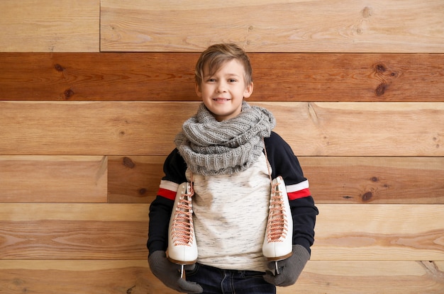 Mignon petit garçon avec des patins à glace contre bois