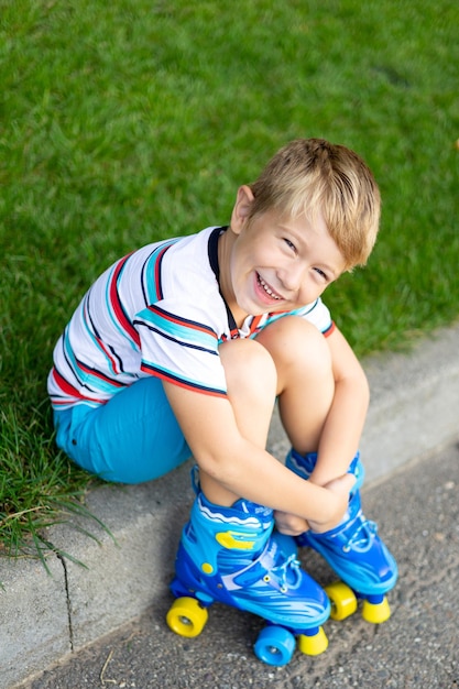 Un mignon petit garçon en patins à roulettes est assis sur l'herbe en souriant en regardant la caméra le concept de sports de plein air jeux actifs