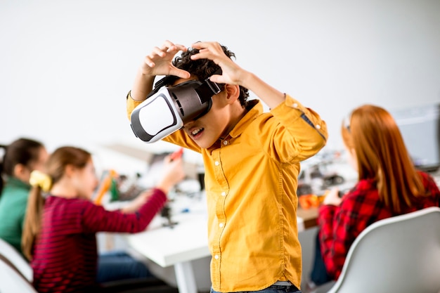 Mignon petit garçon portant des lunettes de réalité virtuelle VR dans une salle de classe de robotique