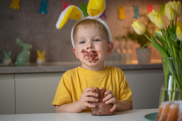 Un mignon petit garçon portant des oreilles de lapin le jour de Pâques mange un lapin de Pâques en chocolat Un enfant joue à la chasse aux œufs pour Pâques Un enfant charmant célèbre Pâques à la maison