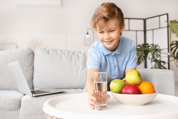 Mignon petit garçon prenant un verre d'eau de table à la maison