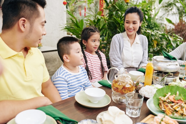 Mignon petit garçon récitant un poème pour la famille lorsqu'il est assis à une grande table à l'extérieur