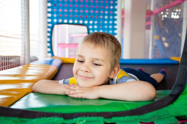 Mignon petit garçon reposant sur un trampoline de terrain de jeu coloré Enfant s'amusant dans un centre de jeu moderne