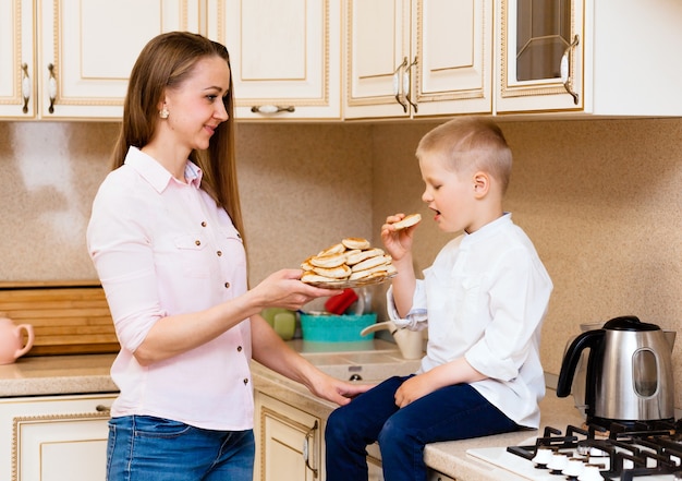 Mignon petit garçon avec sa mère. Famille dans la cuisine. Mère avec fils mangeant des crêpes. pâtisserie maison