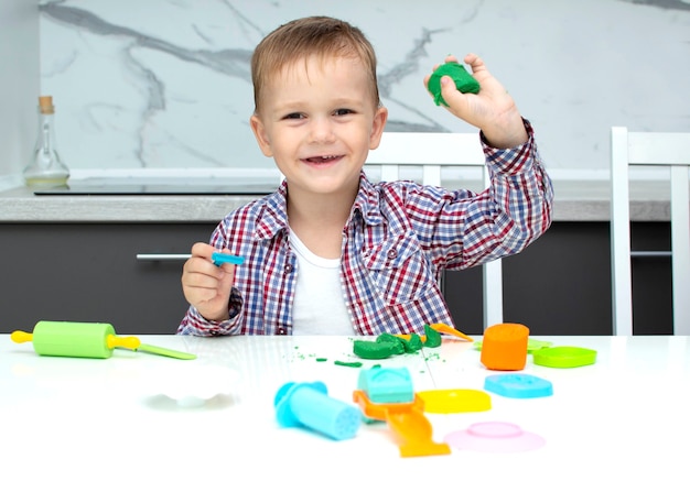 Un mignon petit garçon sculpte de la pâte à modeler sur la table. Le garçon joue dans sa chambre. Jouets éducatifs pour enfants. Jeux pour le développement de l'enfant.Les mains des enfants pétrissent la pâte à modeler.