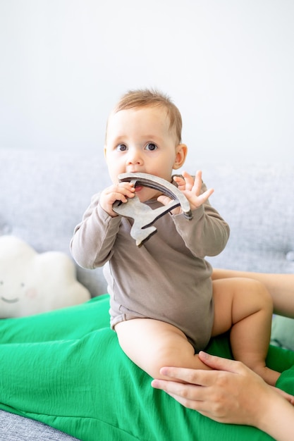 Mignon petit garçon de six mois jouant avec un cheval jouet en bois dans les bras de maman à la maison heureux nouveau-né