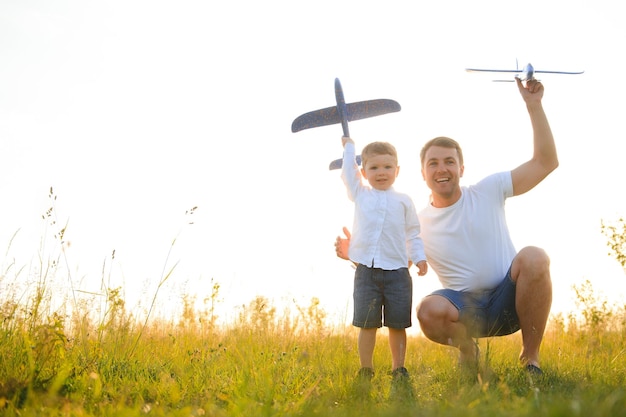 Mignon petit garçon et son beau jeune papa sourient en jouant avec un avion jouet dans le parc